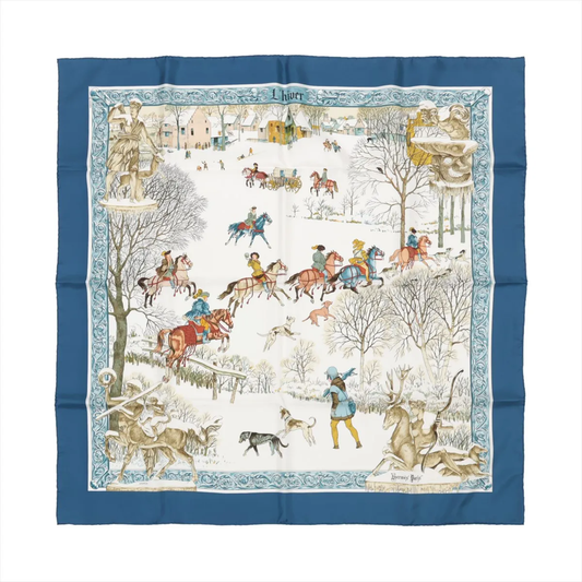 Top-down view of Hermès Carré 90 "L'hiver" silk handkerchief in blue, depicting a detailed winter scene with horse riders, hounds, trees, and snowy landscapes, all bordered by an intricate blue and white frame.
