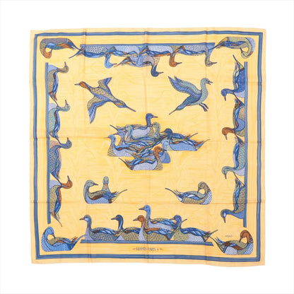Flat-lay image of Hermès Carré 90 "La Mare aux Canards" silk scarf featuring a yellow background with an intricate duck pond motif in blue, orange, and brown tones.