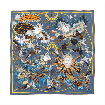 Hermès Carré 90 silk scarf titled "Le Sacre des Saisons," featuring a gray background with an intricate design of fantastical animals, floral patterns, and seasonal symbols in vibrant blue, gold, orange, and white hues, bordered in navy and yellow.