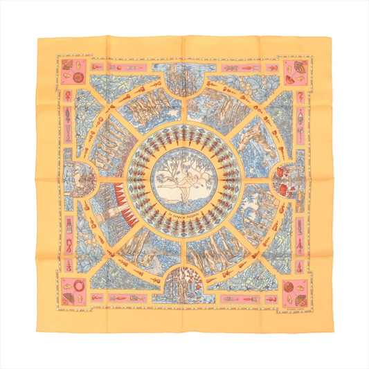 Top-down view of an Hermès Carré 90 "Le Songe de Poliphile" silk handkerchief in orange, featuring a detailed circular illustration with classical motifs in blue, red, and cream tones, bordered by geometric and symbolic artwork.