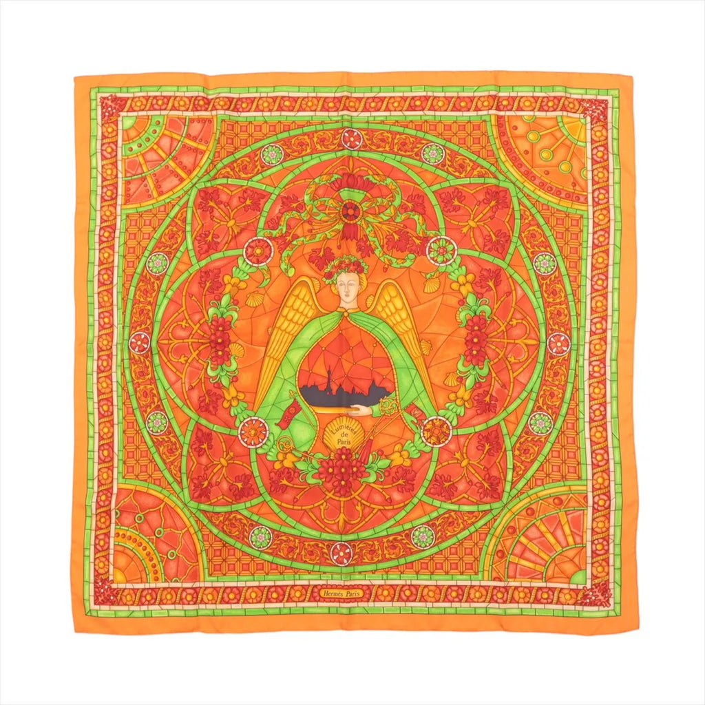 Hermès Carré 90 orange silk scarf with stained-glass style design featuring a central winged figure, green scrollwork, and intricate floral and geometric border details.