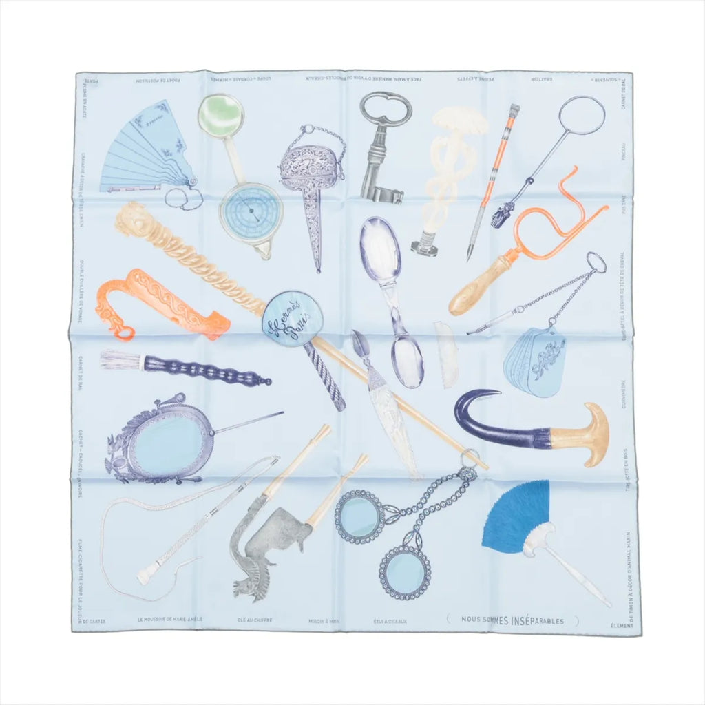 Hermès Carré 90 silk scarf in light blue with illustrated objects and accessories in pastel tones, laid flat on white background.