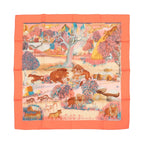 Hermès Carré 90 “Nuba Mountain” silk scarf in orange with multicolor landscape print featuring lions, birds, and foliage.