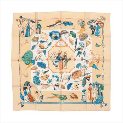 Hermès Carré 90 silk handkerchief in beige featuring a detailed "Ombrelles et Parapluies" design with colorful parasols, umbrellas, and Victorian-era figures, bordered with decorative tassels and elegant illustrations.