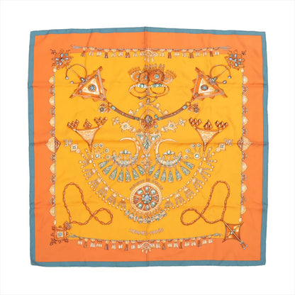Hermès Carré 90 silk scarf titled "Parures des Sables," showcasing intricate illustrations of traditional Saharan jewelry in gold, turquoise, and amber tones on a vibrant orange background with a teal border, creating a rich and ornamental design.