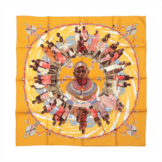 Hermès Carré 90 "Perles du Kenya" silk scarf in orange, featuring a central portrait and a circular design of traditionally dressed figures with colorful beaded adornments.