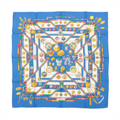 Hermès Carré 90 "Petite Main" silk handkerchief in vibrant blue with detailed illustrations of buttons, sewing tools, and colorful geometric patterns, made from smooth silk and displayed flat against a white background.