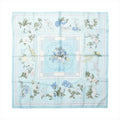 Hermès Carré 90 light blue silk scarf with white, blue and yellow flowers, green leaves and a horse-drawn flower cart at the centre.