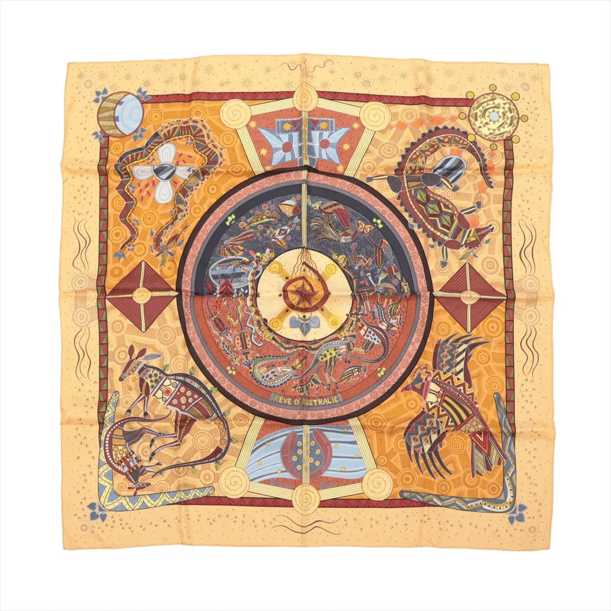 Hermès Carré 90 "Rêve d’Australie" silk handkerchief in beige, showcasing detailed Aboriginal-style artwork of kangaroos, birds, fish, and celestial patterns in earthy tones of red, blue, and ochre, laid flat against a white background.