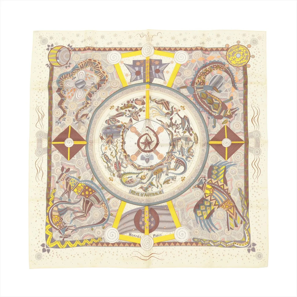 Hermès Carré 90 beige silk scarf with intricate illustrated Australian motifs in earthy tones, yellow accents, and a central circular medallion design.