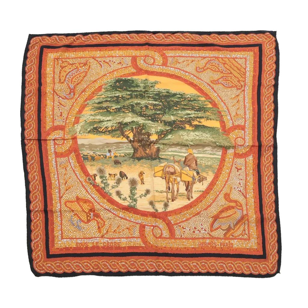 Hermès Carré 90 “Sous Le Cèdre” silk scarf in brown with orange mosaic-style border and central pastoral scene with a large cedar tree, laid flat on white background.