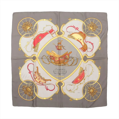 Hermès Carré 90 silk scarf titled "Springs," featuring detailed illustrations of golden and red horse-drawn carriages and harnesses arranged symmetrically on a light gray and taupe background, bordered with intricate gold wheel motifs.