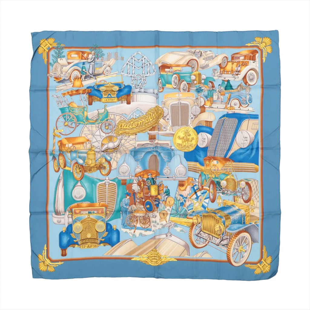 Hermès Carré 90 "St. Christophe et l’Enfant" silk scarf in blue, showcasing an elaborate collage of vintage automobiles in blue, gold, and orange tones with detailed accents, bordered by golden wings and framed with a soft orange edge.