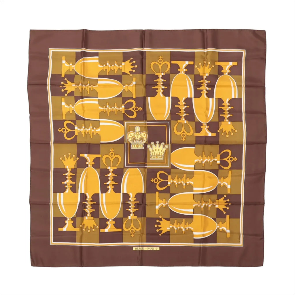 Hermès Carré 90 "ÉCHIQUIER" silk scarf in brown, featuring a symmetrical chessboard-inspired design with alternating light and dark squares, yellow and gold chess pieces, and two central crown emblems in the middle.
