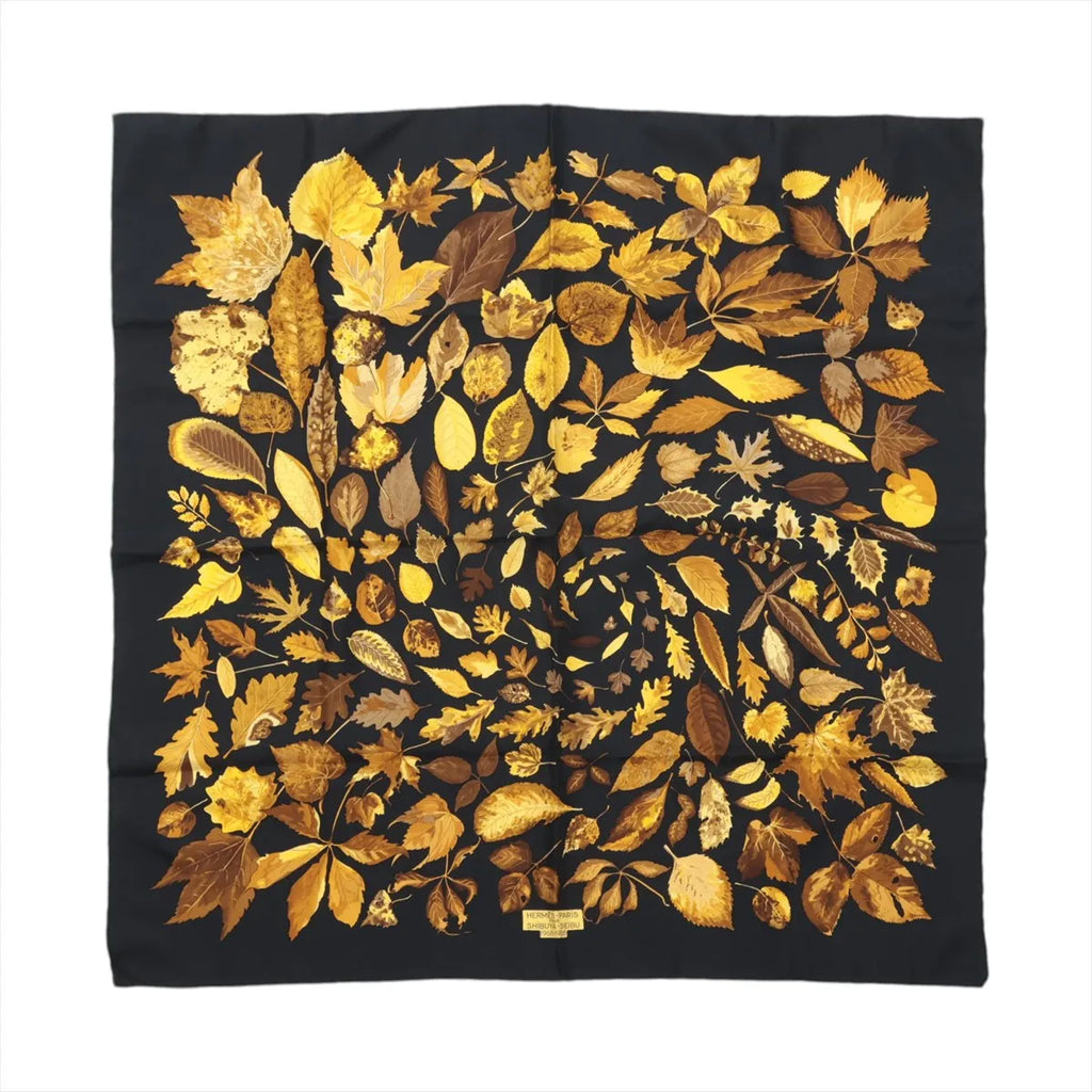 Hermès Carré 90 “Tourbillon” silk scarf in black with golden yellow and brown leaf motif arranged in a spiral pattern.