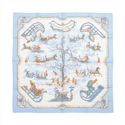 Hermès Carré 90 "Traineaux et Glissades" silk scarf in blue, featuring a central tree surrounded by horse-drawn sleighs, ice skaters, and winter motifs in soft orange, white, and grey tones with a blue and cream border.