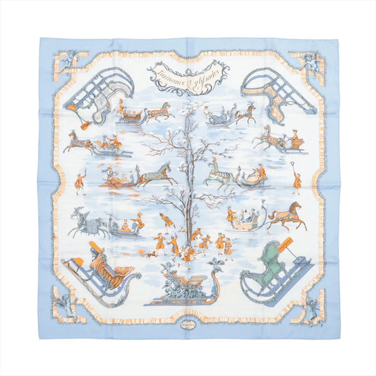 Hermès Carré 90 "Traineaux et Glissades" silk scarf in blue, featuring a central tree surrounded by horse-drawn sleighs, ice skaters, and winter motifs in soft orange, white, and grey tones with a blue and cream border.