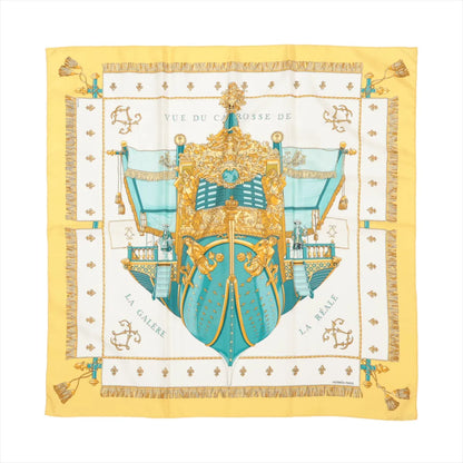 Hermès Carré 90 silk scarf titled "Vue du Carrosse de la Galère La Réale," featuring an ornate baroque ship in turquoise and gold with intricate detailing, surrounded by nautical motifs and tassels, set against a white background with a rich yellow border.
