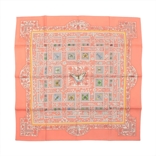 Flat-lay of a Hermès Carré 90 "Joyaux de l'Été" silk scarf in pink, featuring a symmetrical floral and butterfly motif in pastel shades with intricate detailing and a soft coral border.