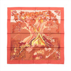 Hermès Kuggor Tree square scarf laid flat, with a coral-red border and a fantastical tree, mushrooms and plants in orange, yellow and burgundy tones.