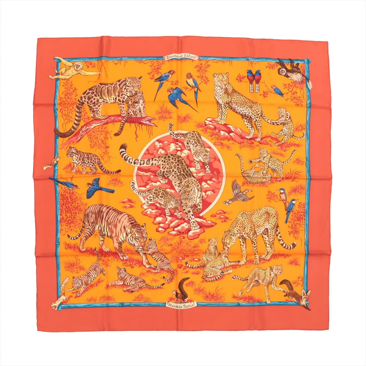 Hermès Carré 90 "Tendresse Feline" silk handkerchief in bright orange, illustrated with leopards, tigers, cubs, and colorful birds in a lush jungle setting, bordered in red-orange with a blue trim, laid flat against a white background.