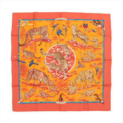 Hermès Carré 90 "Tendresse Feline" silk handkerchief in bright orange, illustrated with leopards, tigers, cubs, and colorful birds in a lush jungle setting, bordered in red-orange with a blue trim, laid flat against a white background.