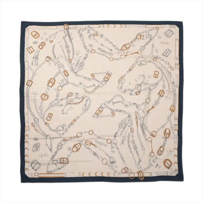 Flat-lay of a Hermès Carré Géant "Malines Chevaux Déchène" scarf in beige with navy blue border, featuring detailed line drawings of horses formed by intertwined bridles and tack in gray and gold tones, printed on a soft cashmere and silk blend.
