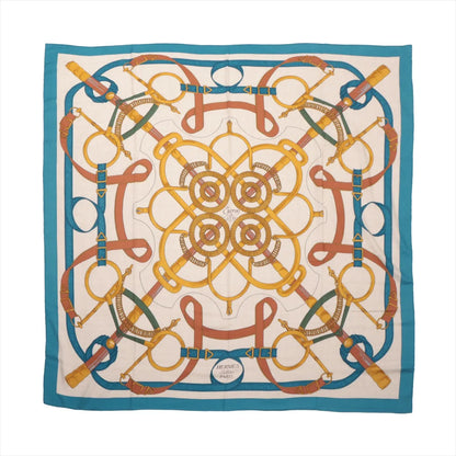 Hermès Carré Géant "Éperon d’Or Golden" handkerchief in a blue and beige colorway, made from a cashmere and silk blend, showcasing intricate golden equestrian gear and symmetrical strap patterns, laid flat against a white background.