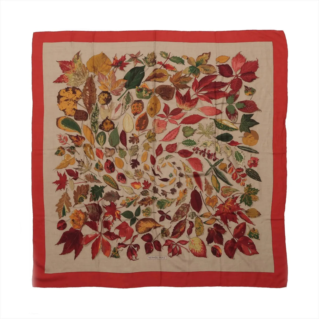 Hermès Carré Géant scarf with beige center, multicolor autumn leaf print in red, gold, green and brown, and a wide red border.
