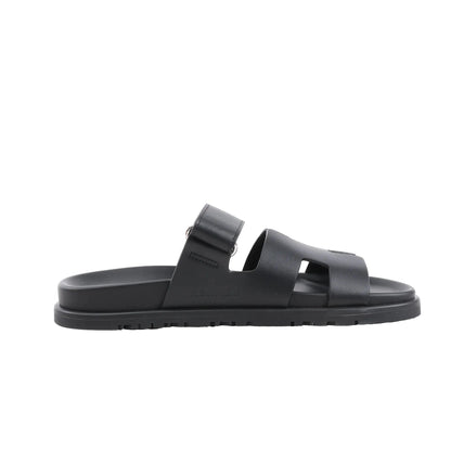 HERMÈS Cypre Leather Sandals in Black, Size 38.5 EU, featuring a smooth black leather upper with adjustable strap, signature “H” cut-out design, contoured footbed, and textured rubber sole, shown in a side profile against a white background.