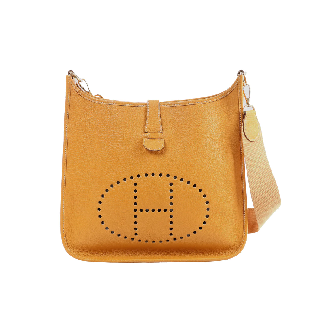Camel brown pebbled leather Hermès Evelyne GM shoulder bag with perforated H logo and beige canvas strap on white background.