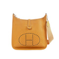 Camel brown pebbled leather Hermès Evelyne GM shoulder bag with perforated H logo and beige canvas strap on white background.