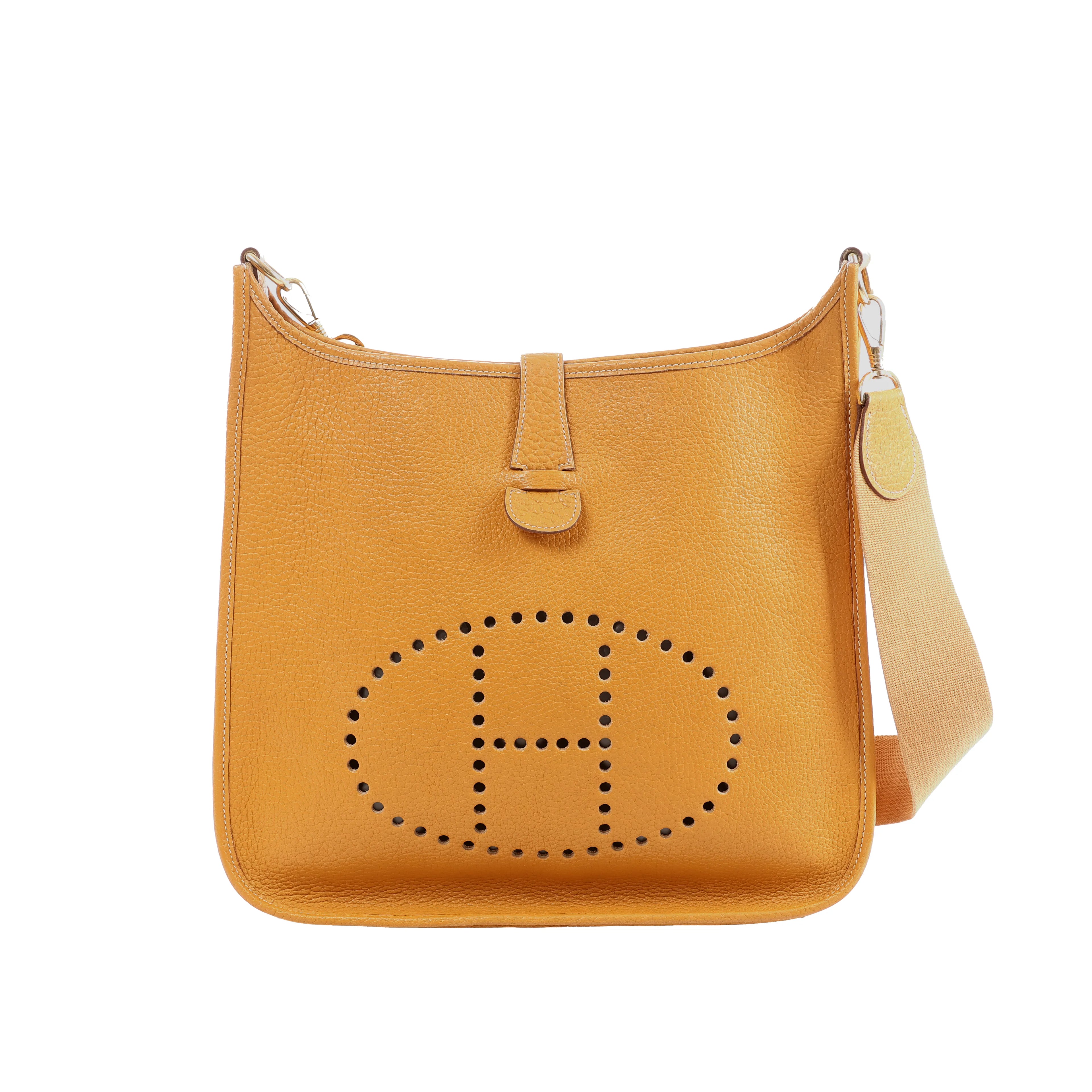Camel brown pebbled leather Hermès Evelyne GM shoulder bag with perforated H logo and beige canvas strap on white background.