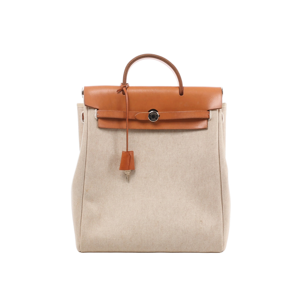 A beige canvas Hermès Herbag Ado PM backpack with a brown leather top flap, handle, closure strap, and hanging key clochette.