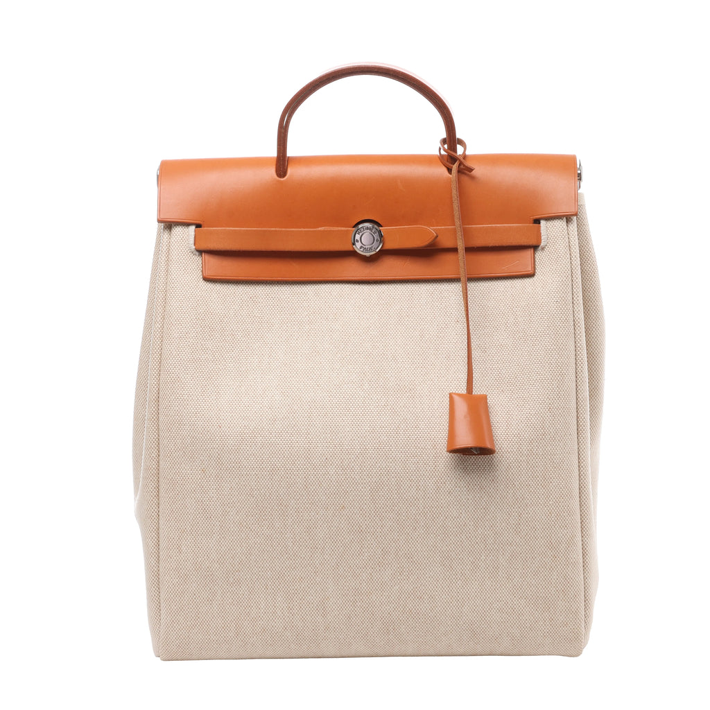 Beige Hermès Herbag Ado PM canvas backpack with brown leather flap, top handle, strap closure and hanging leather clochette.