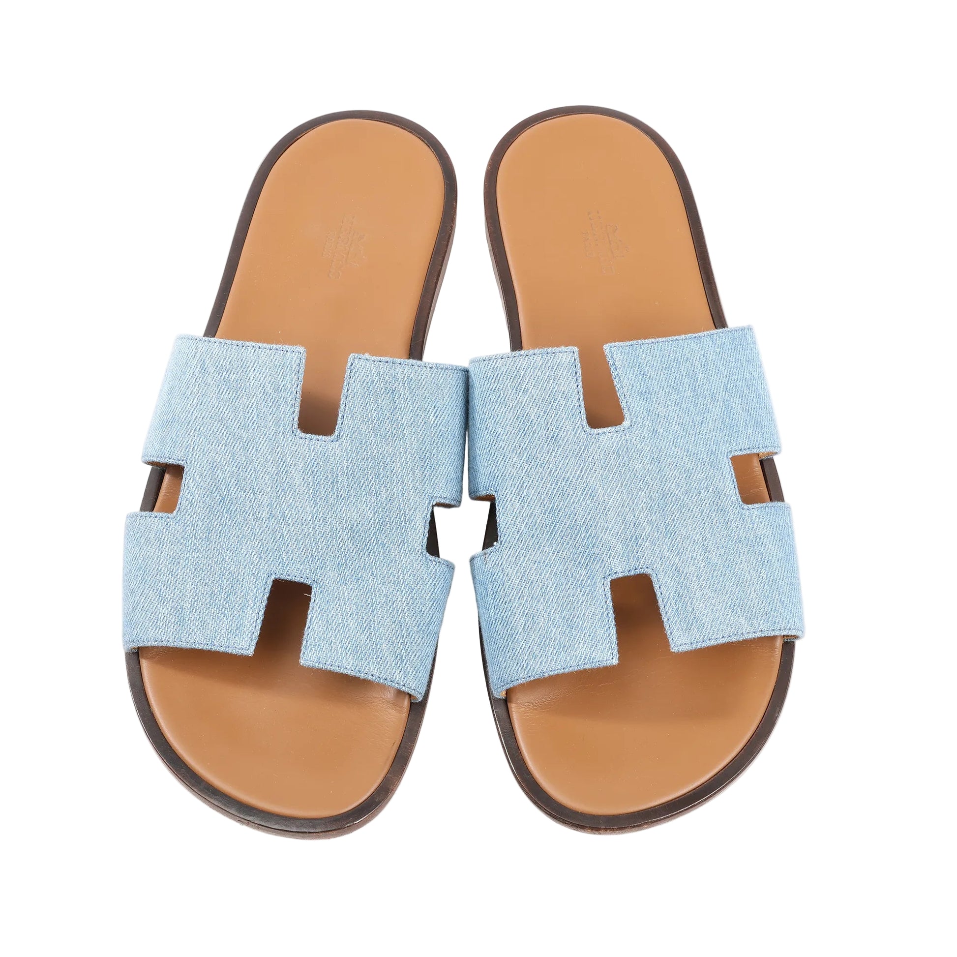 Hermès Izmir sandals in light blue denim featuring wide straps with the signature “H” cut-out design, tan leather footbeds, and dark brown soles. Top view, size 43 EU.