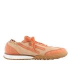 Pair of Hermès Jett sneakers in beige and orange suede with orange laces and textured rubber soles, photographed from the front.