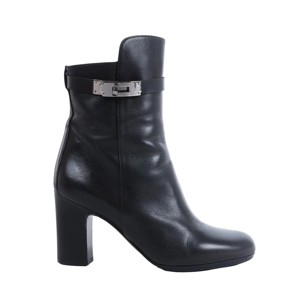 Pair of black Hermès Juez leather ankle boots with block heels and silver-tone buckle straps, displayed beside an orange Hermès box and cream dust bag.