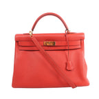 Front view of a red grained leather Hermès Kelly 40 with a top handle, matching shoulder strap, gold-tone turn-lock hardware and hanging leather clochette.