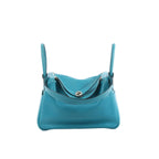 Hermès Lindy 30 handbag in turquoise leather with two top handles, silver-tone turn-lock hardware, and zip-top compartments on a white background.