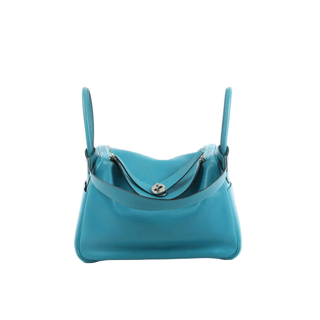 Hermès Lindy 30 handbag in turquoise leather with two top handles, silver-tone turn-lock hardware, and zip-top compartments on a white background.