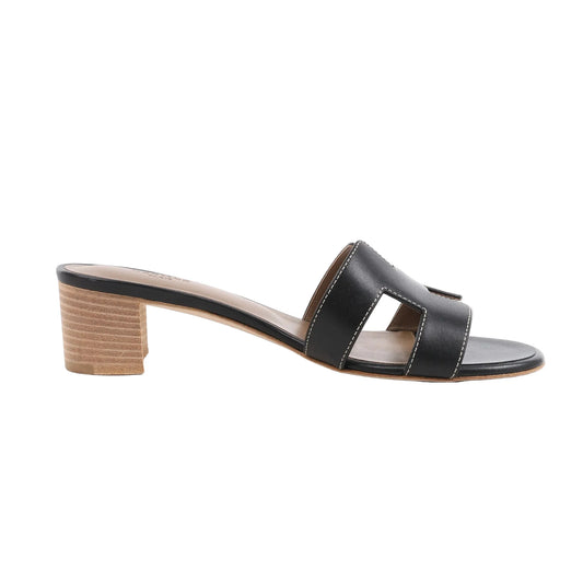 HERMES OASIS black leather slide sandals featuring iconic “H” cutouts, white contrast stitching, and a natural stacked block heel, shown in a side profile against a white background.