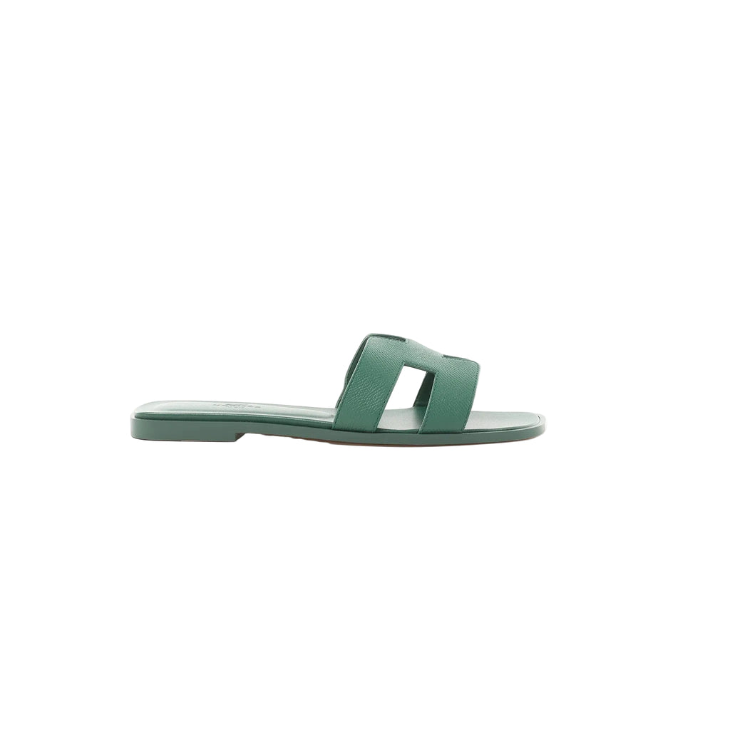 Side view of Hermès Oran slide sandal in Vert Cactus green Epsom leather with H-cutout strap and flat sole on a white background.