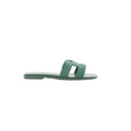 Side view of Hermès Oran slide sandal in Vert Cactus green Epsom leather with H-cutout strap and flat sole on a white background.