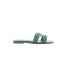 Side view of Hermès Oran slide sandal in Vert Cactus green Epsom leather with H-cutout strap and flat sole on a white background.