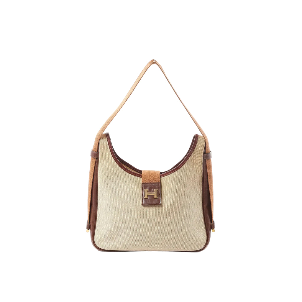 Front view of Hermès Sako shoulder bag in beige Toile H canvas with brown leather trim, long tan strap, and front leather tab with gold-tone H detail.