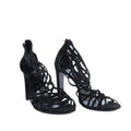 Pair of black Hermès strappy high-heel sandals with open toes and intricate lattice-style uppers, photographed from the front.