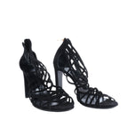 Pair of black Hermès strappy high-heel sandals with open toes and intricate lattice-style uppers, photographed from the front.