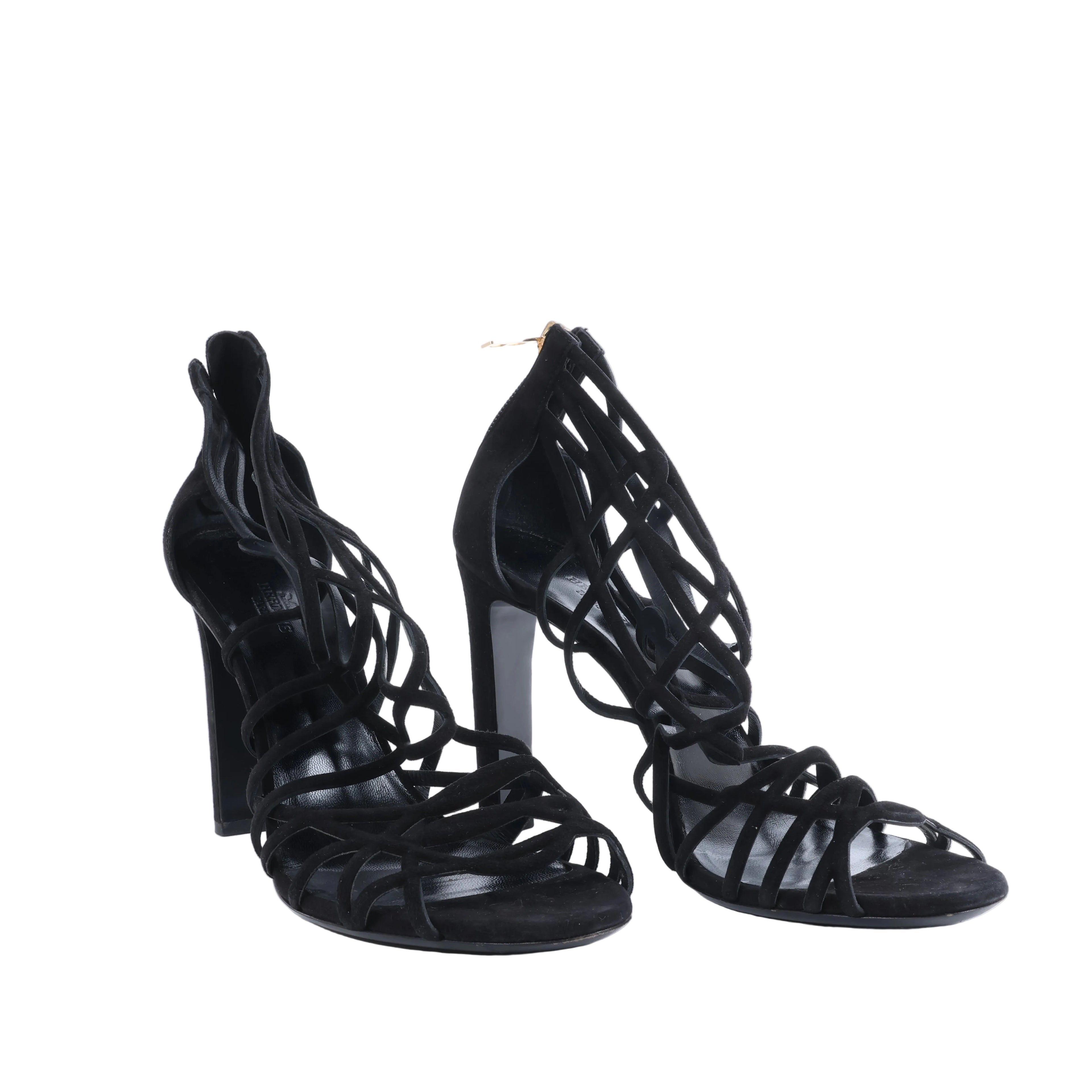 Pair of black Hermès strappy high-heel sandals with open toes and intricate lattice-style uppers, photographed from the front.