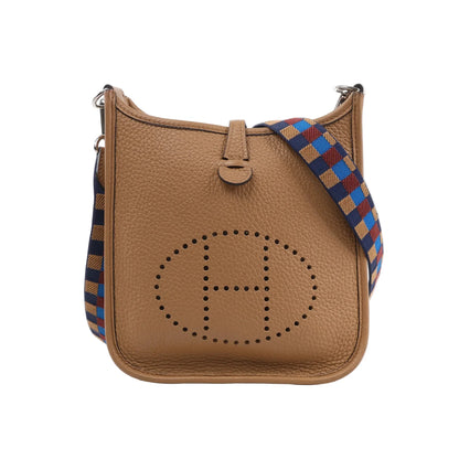 Hermès Evelyne TPM shoulder bag in chai brown Taurillon Clemence leather with perforated “H” logo on the front and a colorful Maxi Quadrille canvas strap in blue, red, and gold tones, shown upright against a white background.